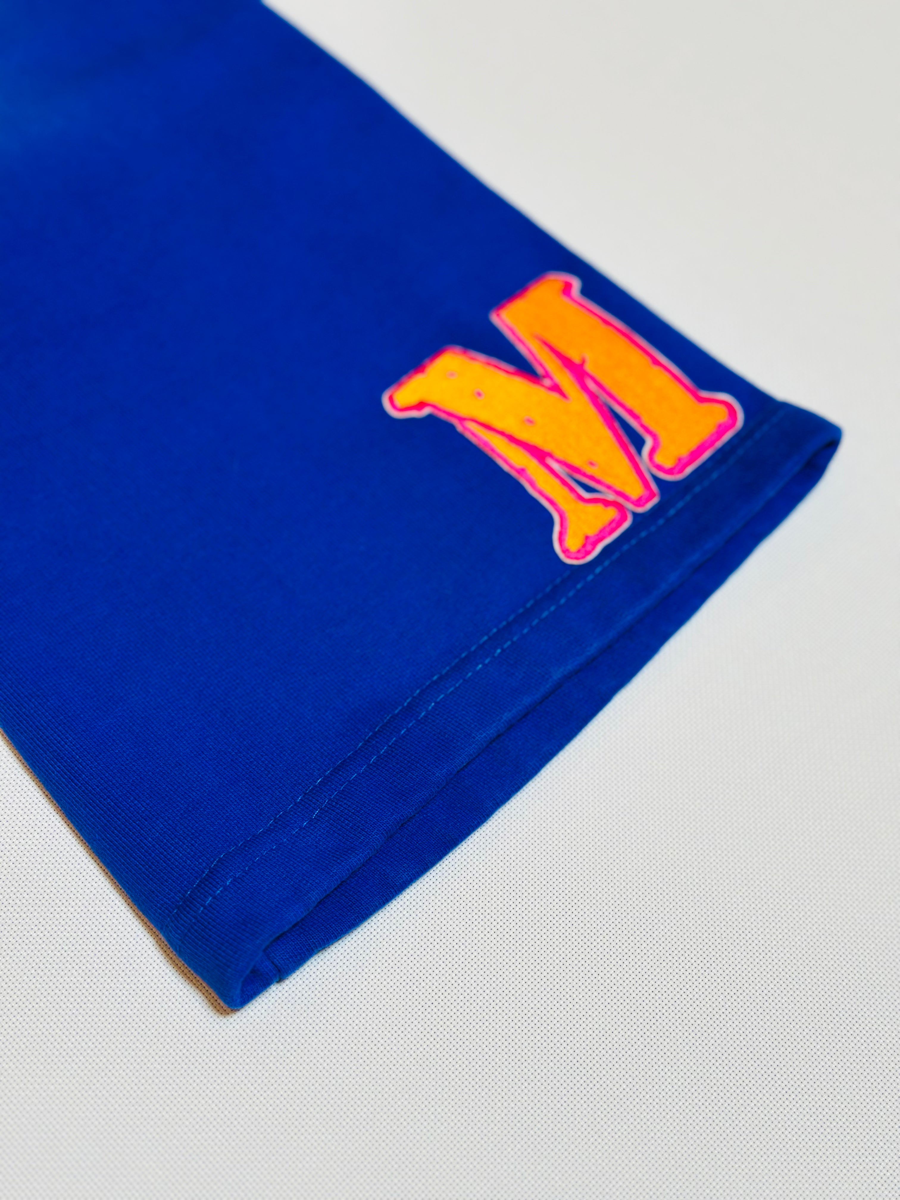Blue fabric with a large orange letter 'M' bottom left front on a light gray background