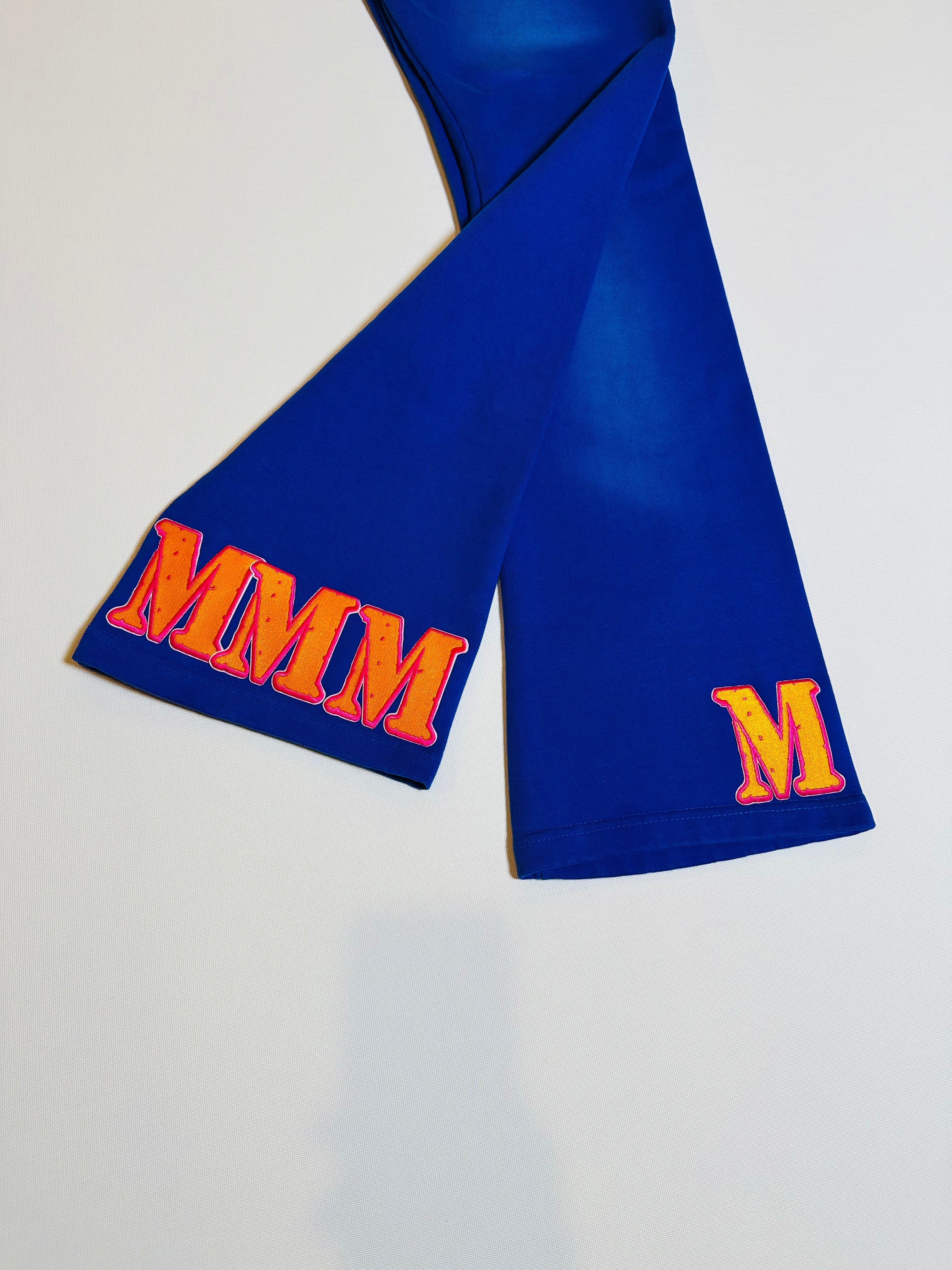 Blue fabric pants with orange letters 'MMM' on a light gray background