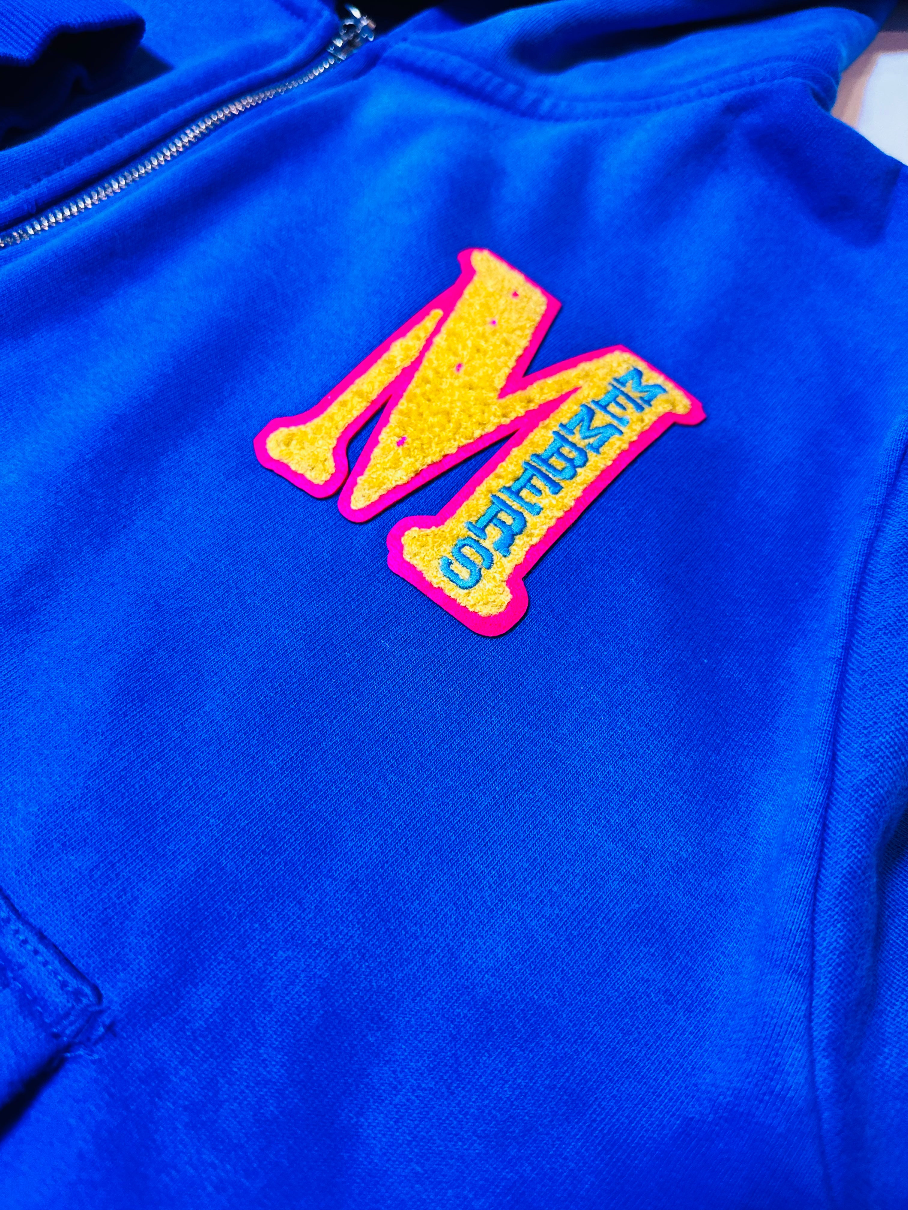Blue jacket with a colorful 'M' logo on a white background