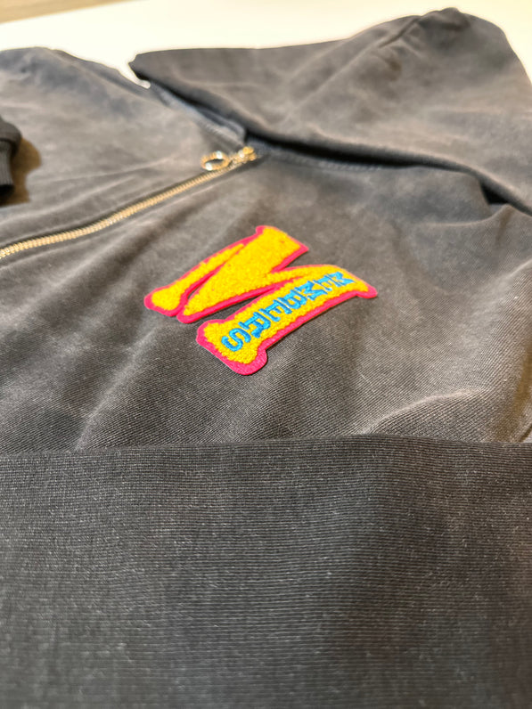 Dark hoodie with a colorful patch on a neutral background
